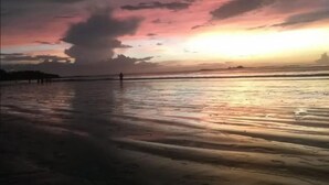 A beach with a sunset, calm water, and a few people walking. - Paradise point camping - Dome 1 (Tamarindo)