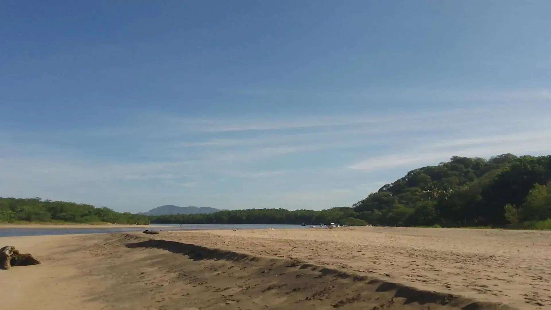Una playa arenosa con cielo despejado y montañas a lo lejos.
