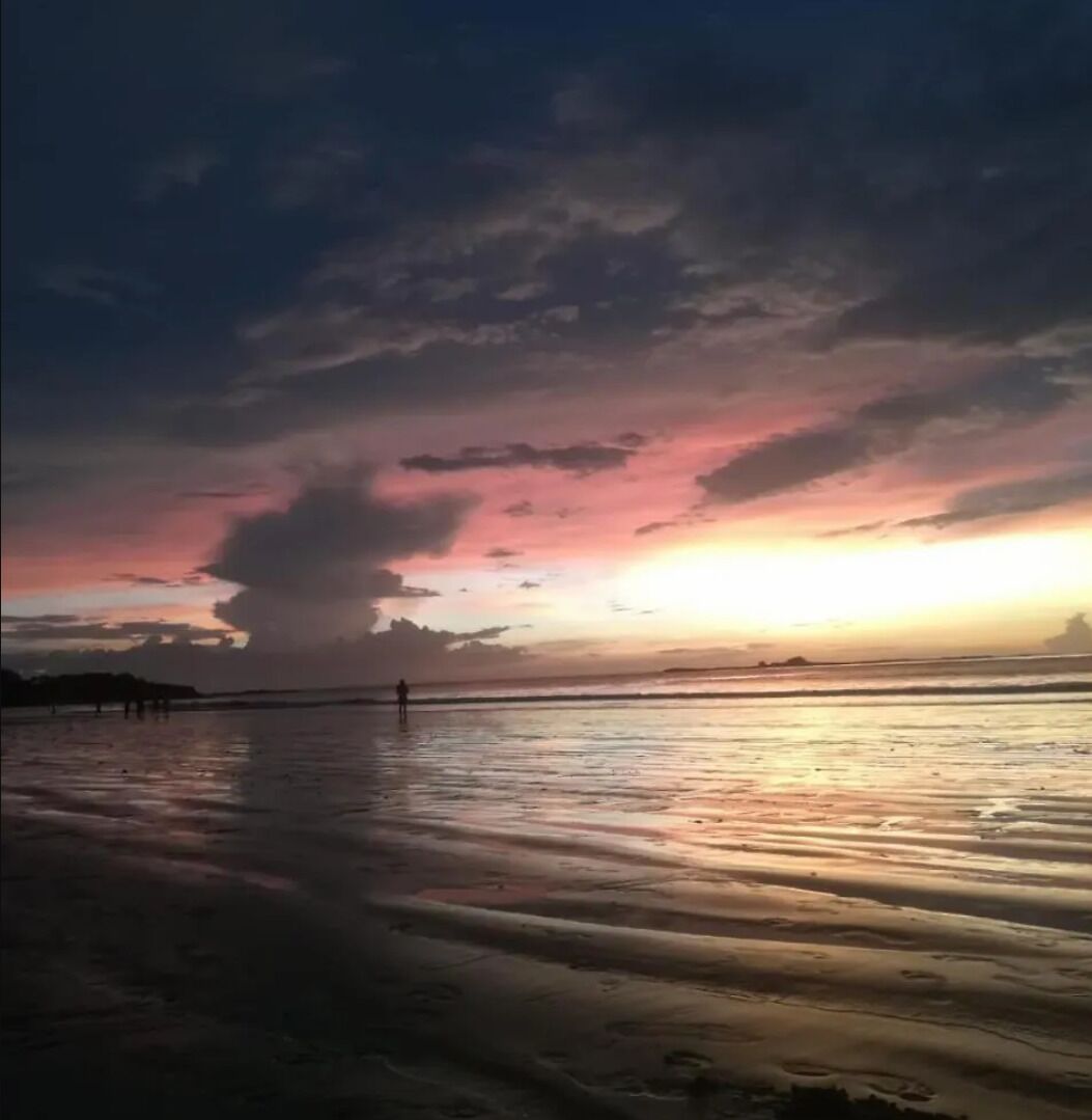 Ein Strand bei Sonnenuntergang, ruhiges Wasser und einige Spaziergänger.