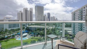 Un balcón con vista a la ciudad, un área de piscina y una silla de descanso.