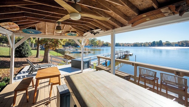 Eine überdachte Terrasse mit Seeblick, Holzmöbel und einem Deckenventilator.
