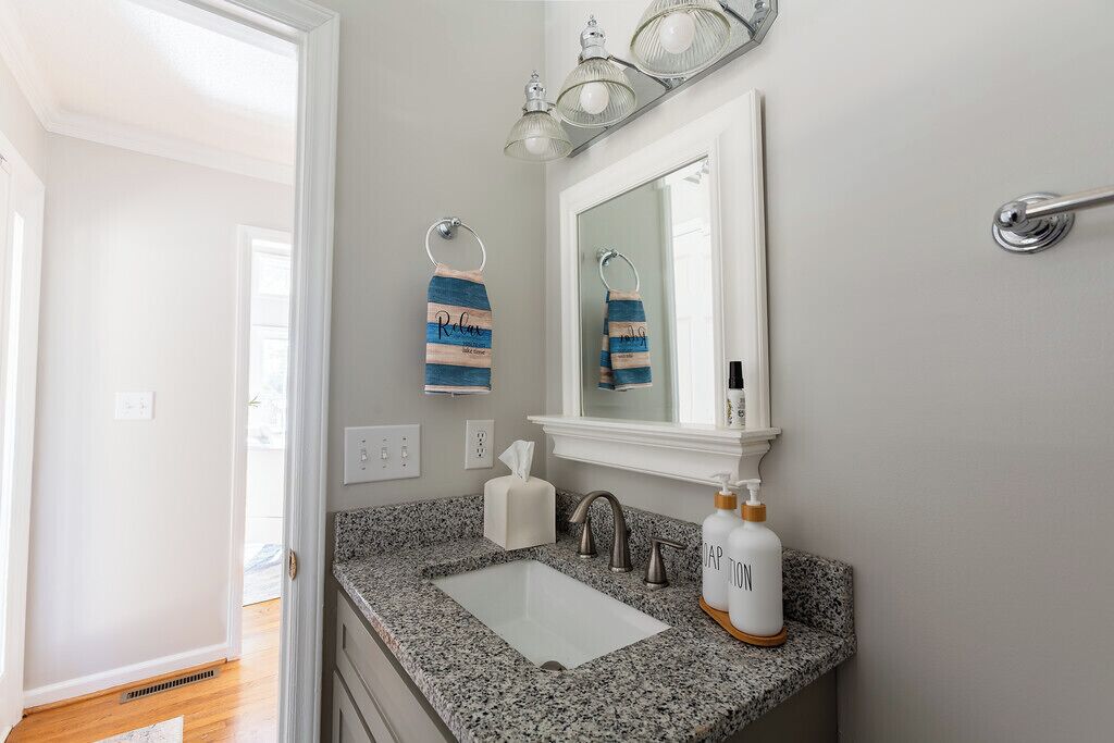 Un bagno con lavabo in granito, uno specchio, un porta asciugamani con asciugamano e un dispenser per sapone.