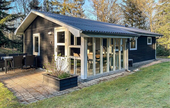 Une maison moderne dotĂ©e dâune grande extension en verre, dâun patio avec mobilier dâextĂ©rieur et dâun jardin bien entretenu.