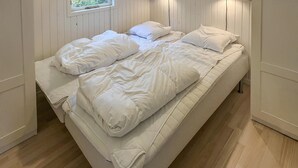 Et enkeltværelse med trægulv, hvide vægge og et vindue med udsigt til grønne områder.