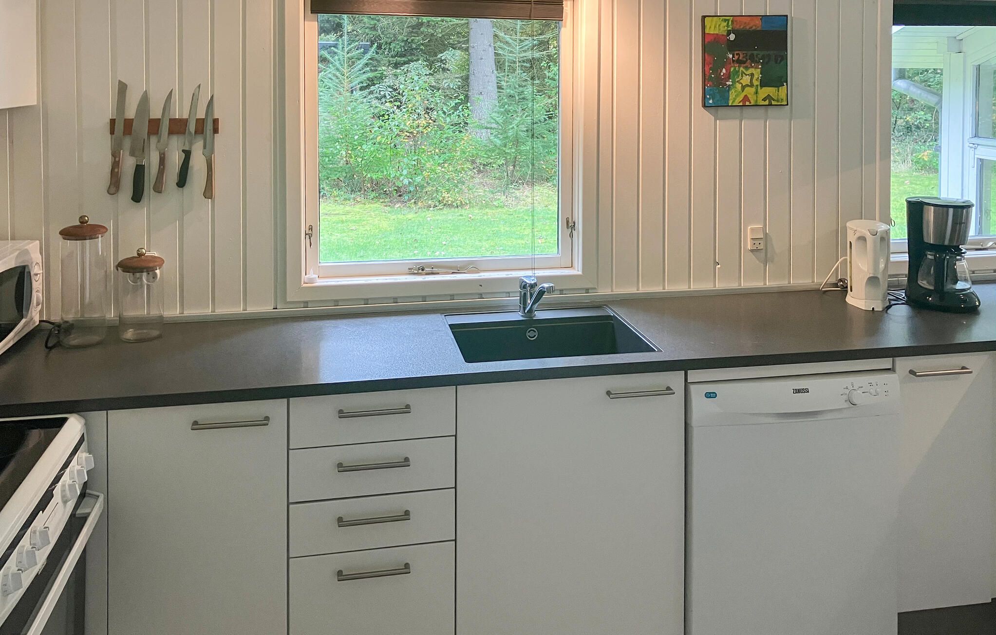 Een keuken met witte kastjes, een zwart aanrecht, een raam met uitzicht op groen en een koffiezetapparaat.