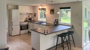 Et moderne køkken med hvide skabe, en central ø, barstole og udsigt til det fri.