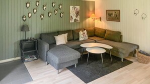 En moderne stue med en hjørnesofa, et lille sofabord, et kaffe- eller sofabord og dekorativ vægkunst, herunder kranier og et maleri.