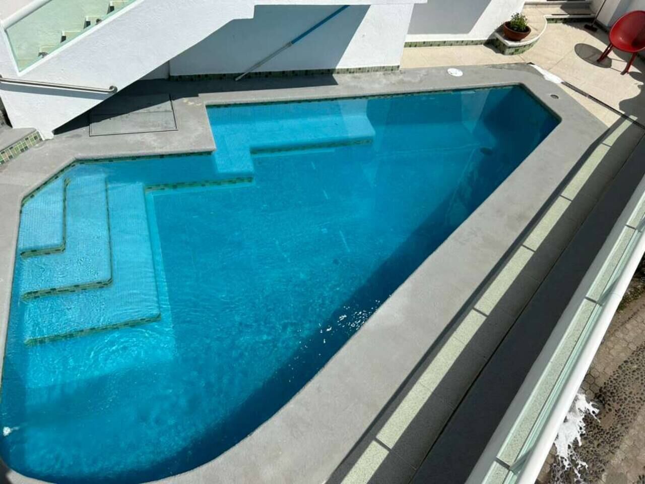 A rectangular swimming pool with a clear blue water, surrounded by a concrete deck and a glass railing.