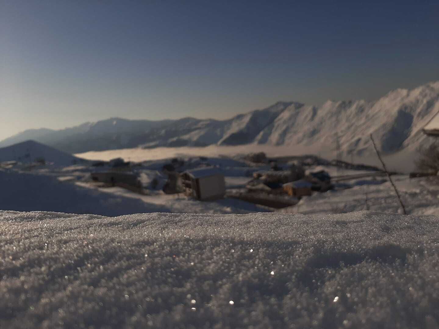 Et snødekt landskab med en lille bebyggelse og bjerge i baggrunden.