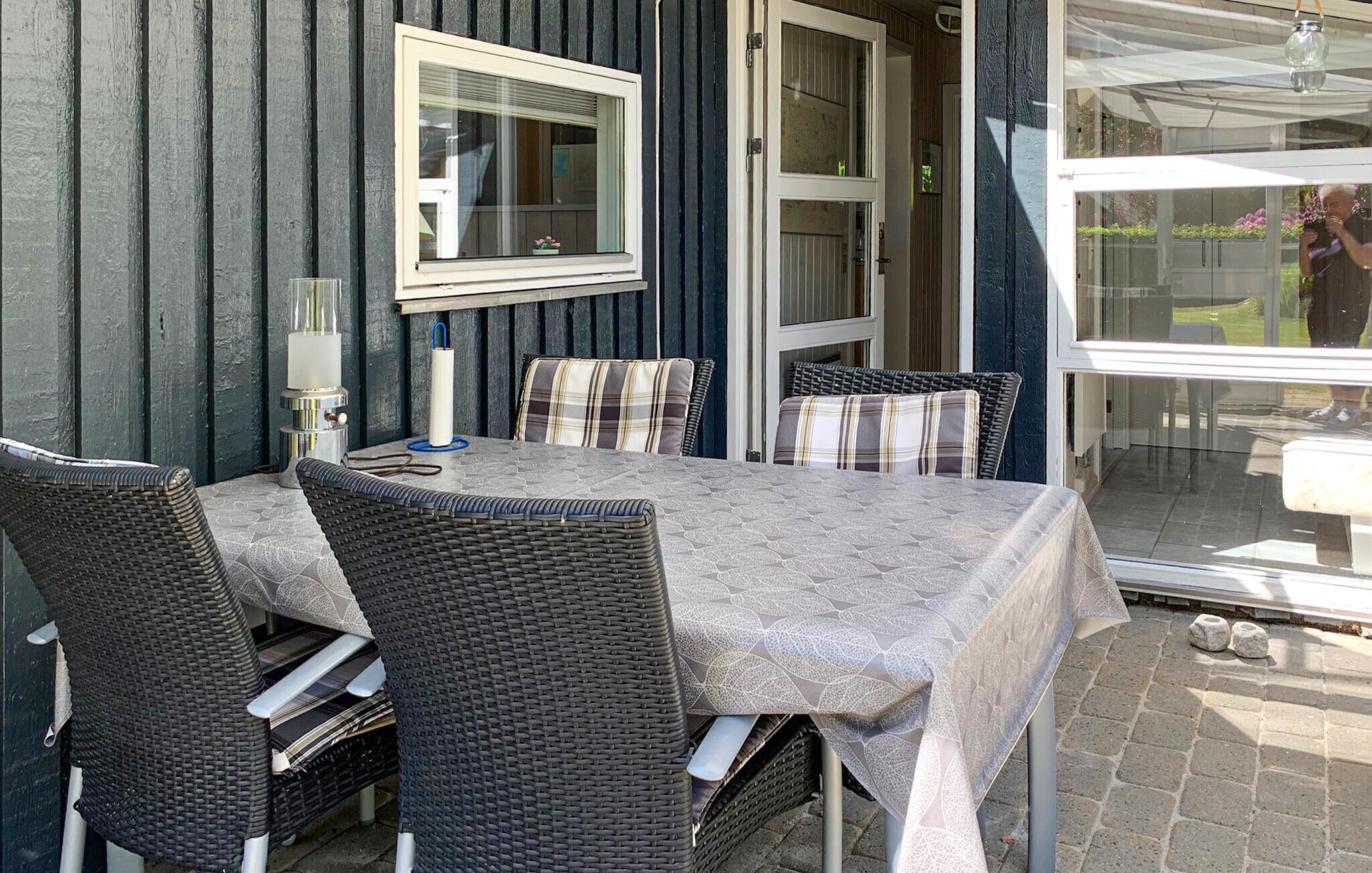 Un espace extérieur aménagé pour les repas, avec des chaises et une table en osier, une fenêtre offrant une vue agréable et une porte donnant sur une autre pièce.