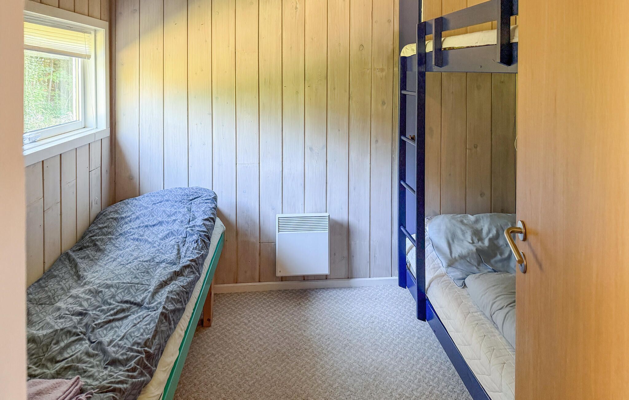 A compact room with two bunk beds, a window with blinds, and a wall-mounted heater.