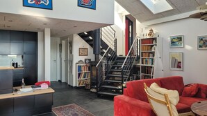 A modern living room with a red sofa, a coffee table, and a bookshelf. A staircase leads to an upper level. - 3 bedroom stunning home in Sunds (Sunds)