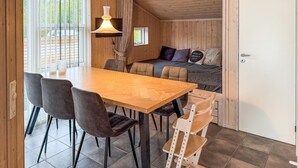 Pieni huone, jossa on puinen ruokapöytä, neljä tuolia, tyynyillä varustettu sänky, riippuvalaisin ja pieni ikkuna.