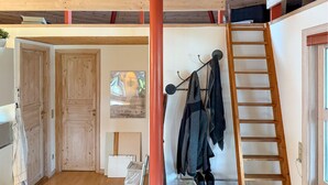 A room with a wooden ceiling, a wooden door, a coat rack with clothes, a ladder, and a window with a view. - Gorgeous home in Hovborg with WiFi (Hovborg)