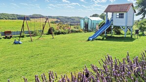 Ein Spielplatz mit Schaukeln, einer Rutsche und einer kleinen Hauskonstruktion.