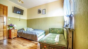 Ein Zimmer mit zwei Betten, einem Holzschrank, einem Fernseher und einem Fenster mit Vorhängen.