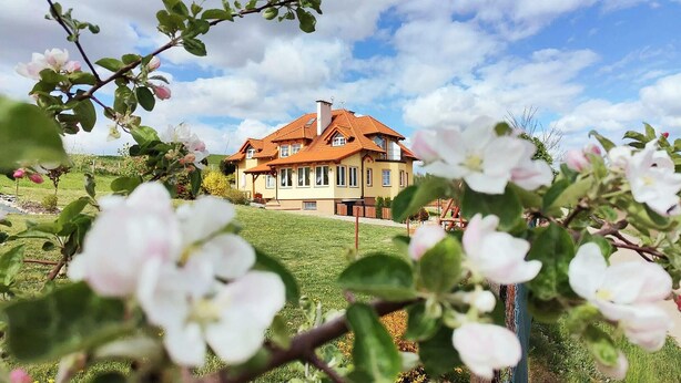 Ein zweistöckiges Haus mit rotem Ziegeldach, umgeben von einer grünen Wiese und blühenden Blumen.