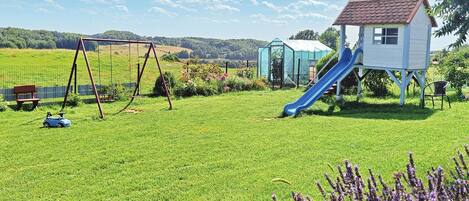 A playground with swings, a slide, and a small house structure.