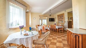 Zona pranzo con tavoli rotondi, sedie in vimini e angolo cottura con pensili in legno.