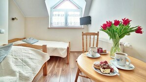 Ein gemütliches Schlafzimmer mit zwei Einzelbetten, einem Holzstuhl, einem Esstisch mit Speisen und Getränken sowie einem Fenster mit Blick.