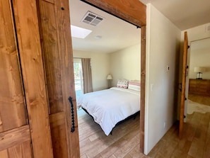 Un dormitorio con cama, piso de madera y una puerta que da a otra habitación.
