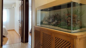 A room with a wooden cabinet housing a fish tank, a bed, and a bathroom visible through an open door. - Luna Apartment - Sea View Private Apartment - AC - WiFi (Faro)