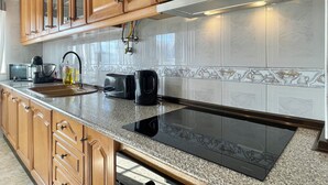 A kitchen with wooden cabinets, a stainless steel range hood, a built-in stovetop, a microwave, a toaster, and a coffee maker. - Luna Apartment - Sea View Private Apartment - AC - WiFi (Faro)