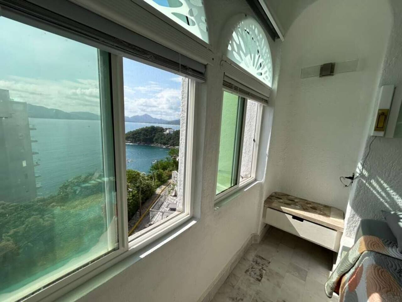 A room with large windows, a bed, and a view of a body of water and distant landscape.