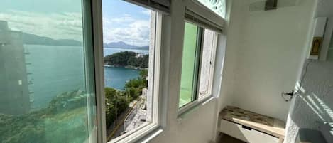A room with large windows, a bed, and a view of a body of water and distant landscape.
