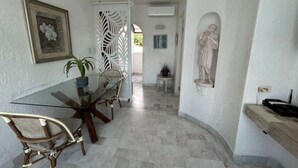 Zona pranzo con tavolo in vetro e sedie, una pianta in vaso, un paravento decorativo e una statua appesa al muro.