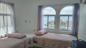 Ein Zimmer mit zwei Betten, einem Fenster mit Blick, einer Lampe und einem Sessel.
