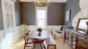A dining area with a wooden table, chairs, a bench, a chandelier, a window, and a white brick wall. - Eclectic, Bright, & Spacious Retreat in the Heart of SLC (Salt Lake City)