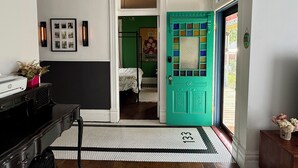 A hallway with a black and white tiled floor, a teal door with a window, and a bed in the adjacent room. - Eclectic, Bright, & Spacious Retreat in the Heart of SLC (Salt Lake City)