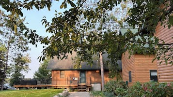 A wooden cabin with a gravel driveway leading to a wooden deck.