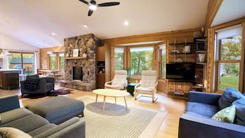 Cozy wood-lined living room with stone fireplace and bright forest views