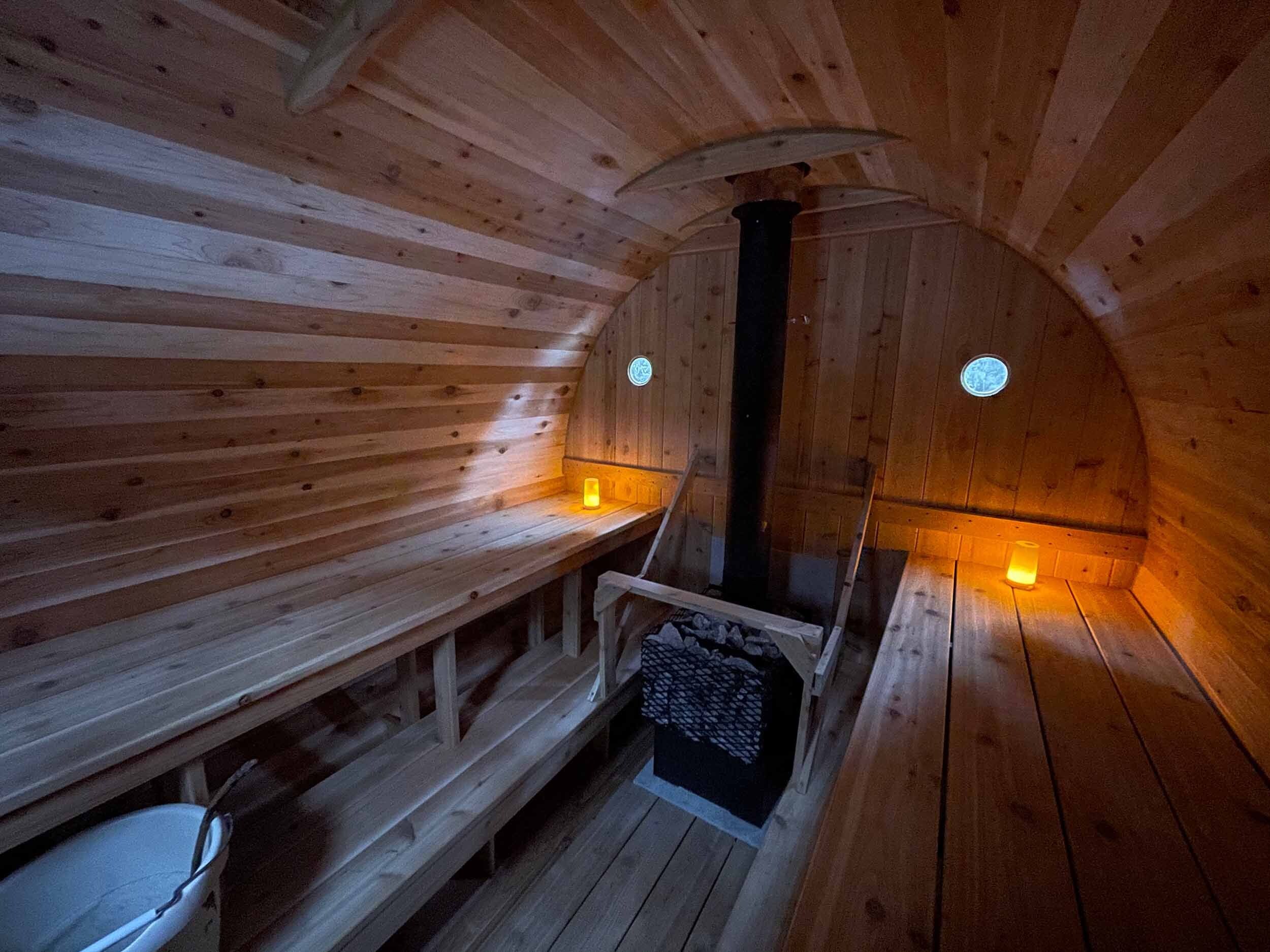 Un sauna avec des murs et des bancs en bois, un pilier central et deux fenêtres rondes.