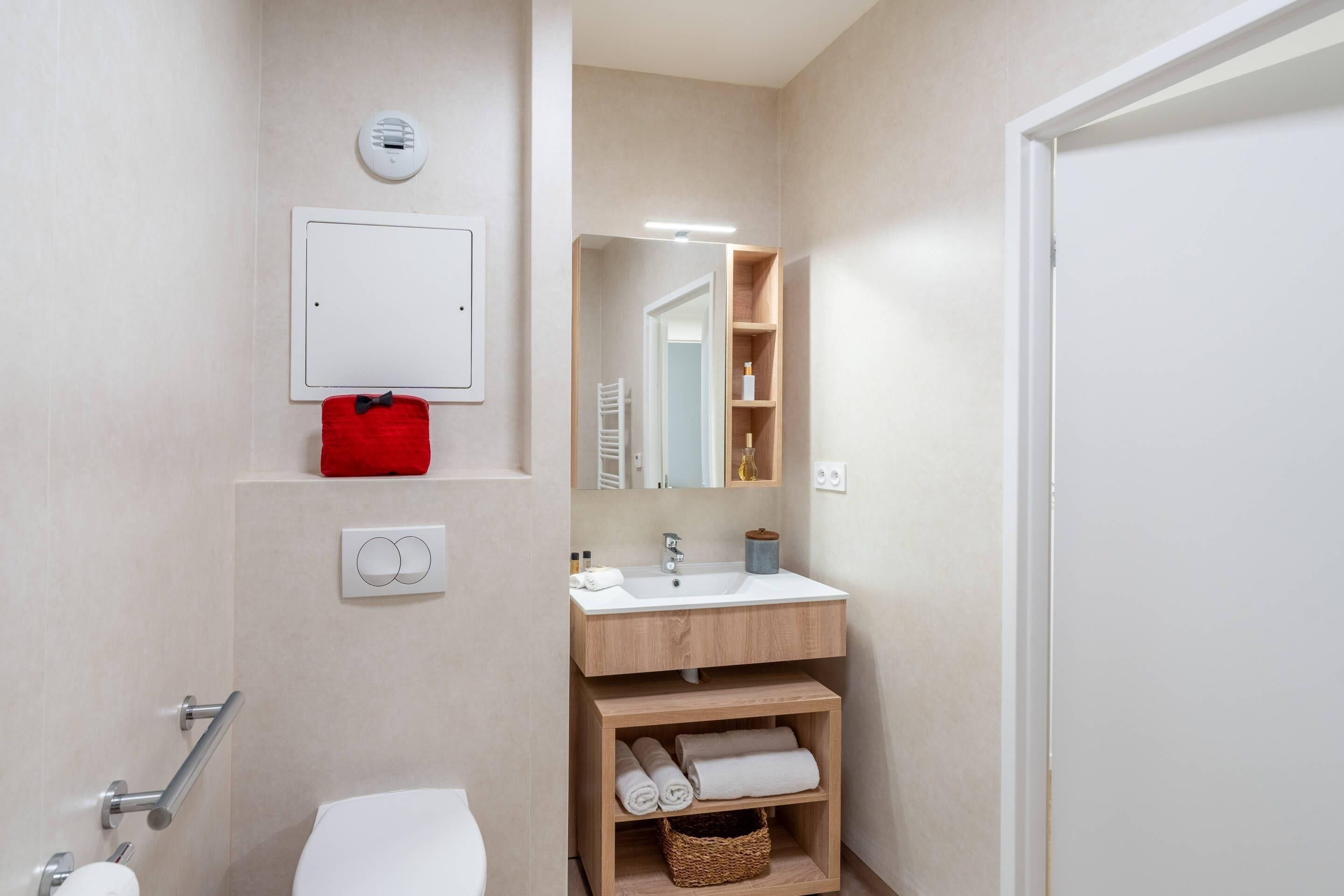 Een moderne badkamer met een wit toilet, een houten wastafelmeubel met een wastafel, een spiegel en een handdoekrek.