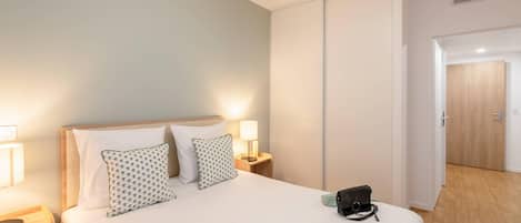 A hotel room with a bed, bedside lamps, a nightstand, a door, and a wooden floor.