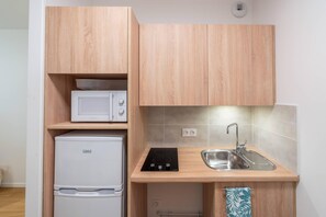 A compact kitchen with wooden cabinets, a microwave, a Linke refrigerator, and a sink with a faucet. - Quality Aparthotel Nancy Zenith (Laxou)
