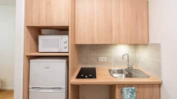 A compact kitchen with wooden cabinets, a microwave, a Linke refrigerator, a sink, and a towel hanging on the cabinet door.