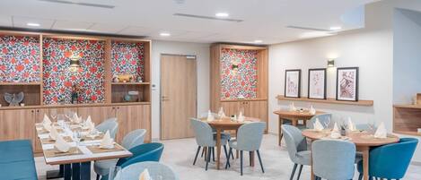 Un restaurante con varias mesas, sillas azules y un diseño floral en la pared.