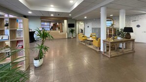 Een ruime lobby met een receptiebalie, een zithoek en een boekenkast.