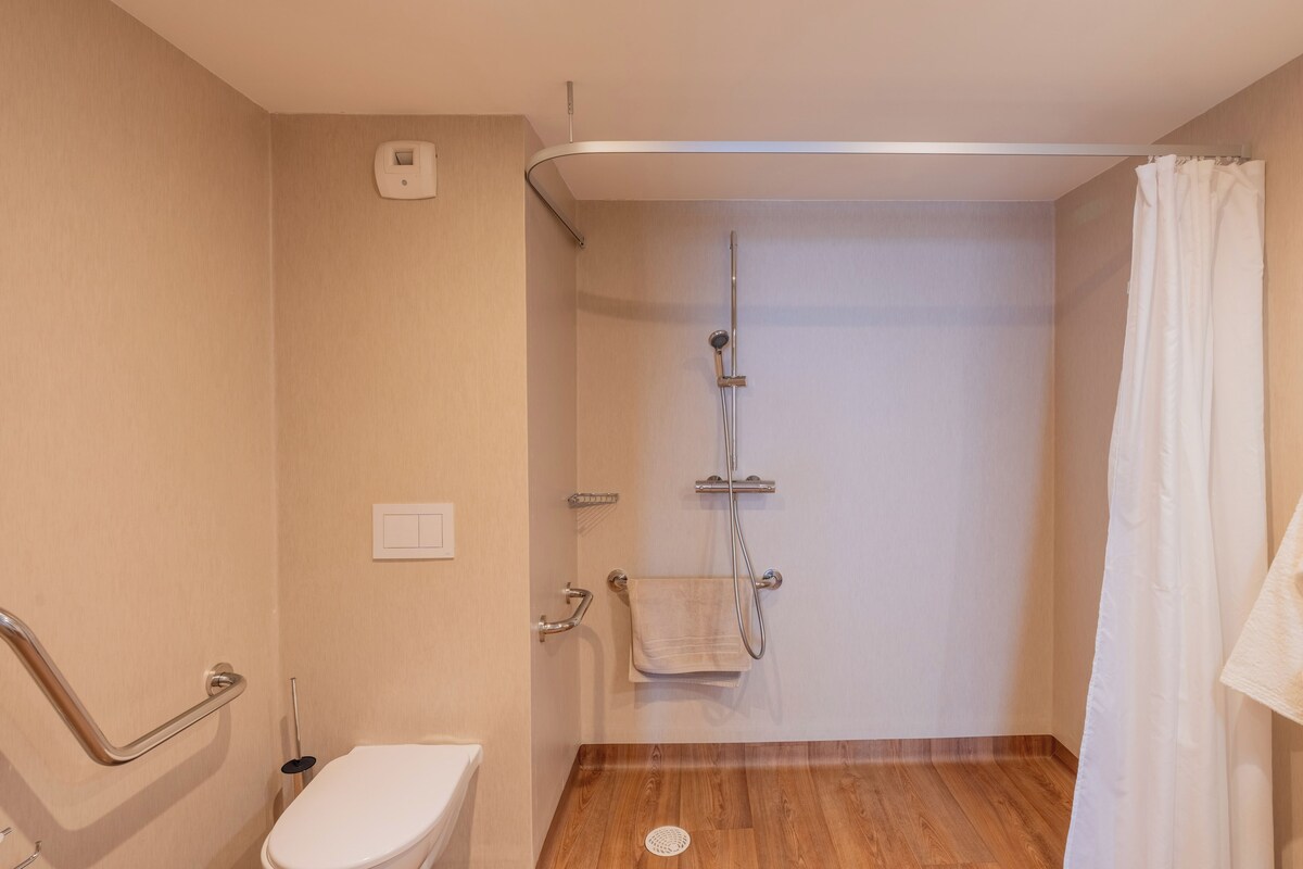 A bathroom with a shower, a toilet, a grab bar, and a towel rack.