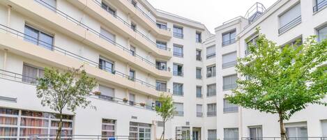 Un edificio residencial moderno de varios pisos con balcones, un patio central y una bicicleta estacionada cerca de la entrada.