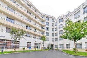 Un immeuble résidentiel moderne à plusieurs étages, doté de balcons, d’une cour intérieure et d’un vélo garé près de l’entrée.