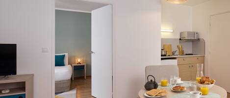 A modern hotel room with a bed, bedside table, and a dining area with breakfast.