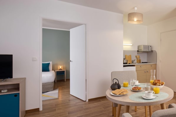 A modern hotel room with a bed, bedside table, and a dining area with breakfast. - Quality Aparthotel Valenciennes (Valenciennes)