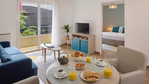 Een moderne hotelkamer met een balkon, een zithoek met ontbijt, een televisie en een bed.