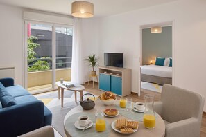 Une chambre d’hôtel moderne avec balcon, un coin repas où le petit-déjeuner est servi, une télévision et un lit.