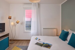 Une chambre d’hôtel équipée d’un lit, d’une télévision, d’un bureau, d’une lampe de chevet et d’une fenêtre avec des rideaux.